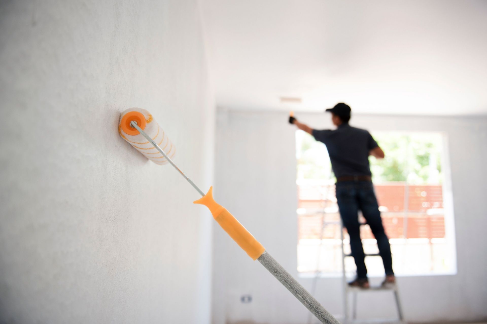 Painter using roller to paint a white wall indoors.