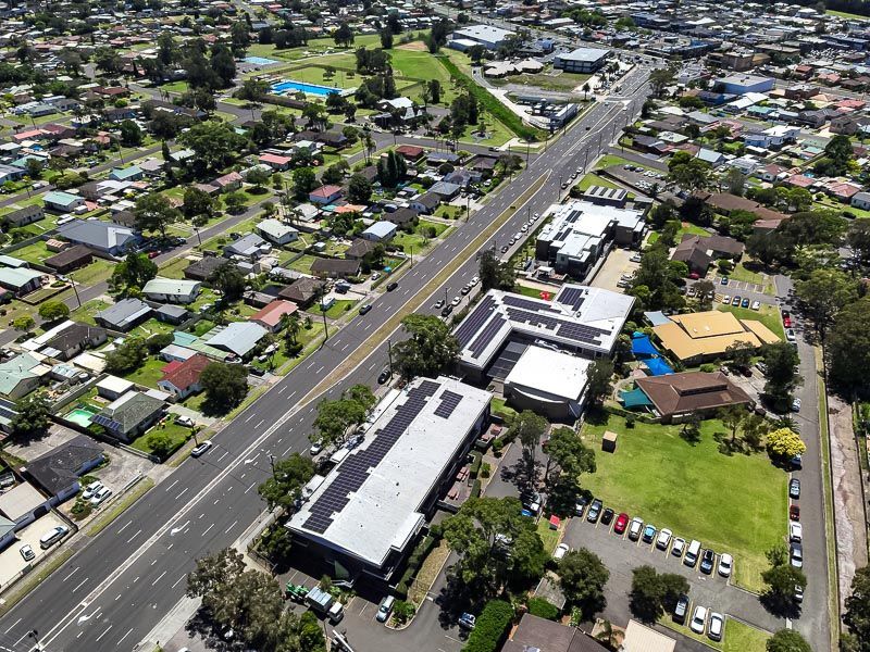Aerial view of a suburban road lined with houses, buildings, and parked cars on a sunny day