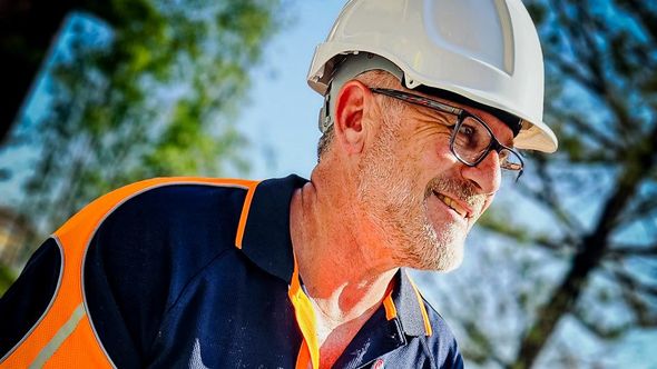 Construction worker in PPE white hardhat smiling looking away from camera