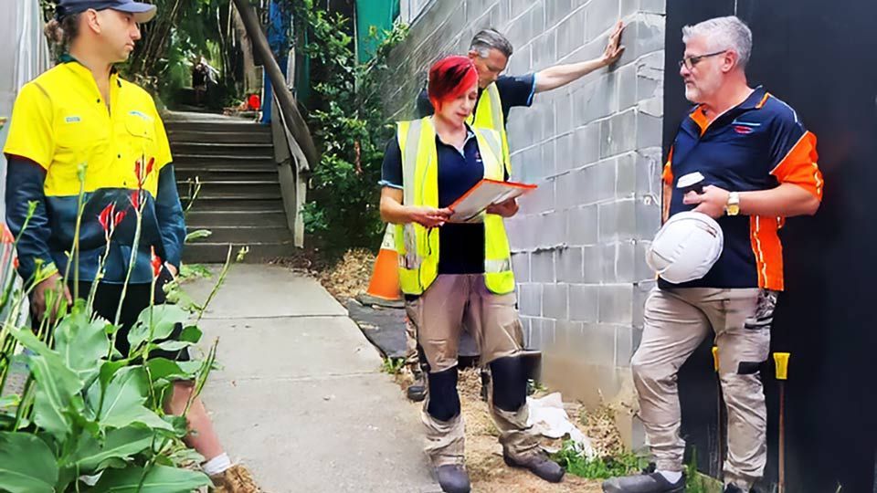 Three workers in safety gear talking beside a cinderblock wall outdoors