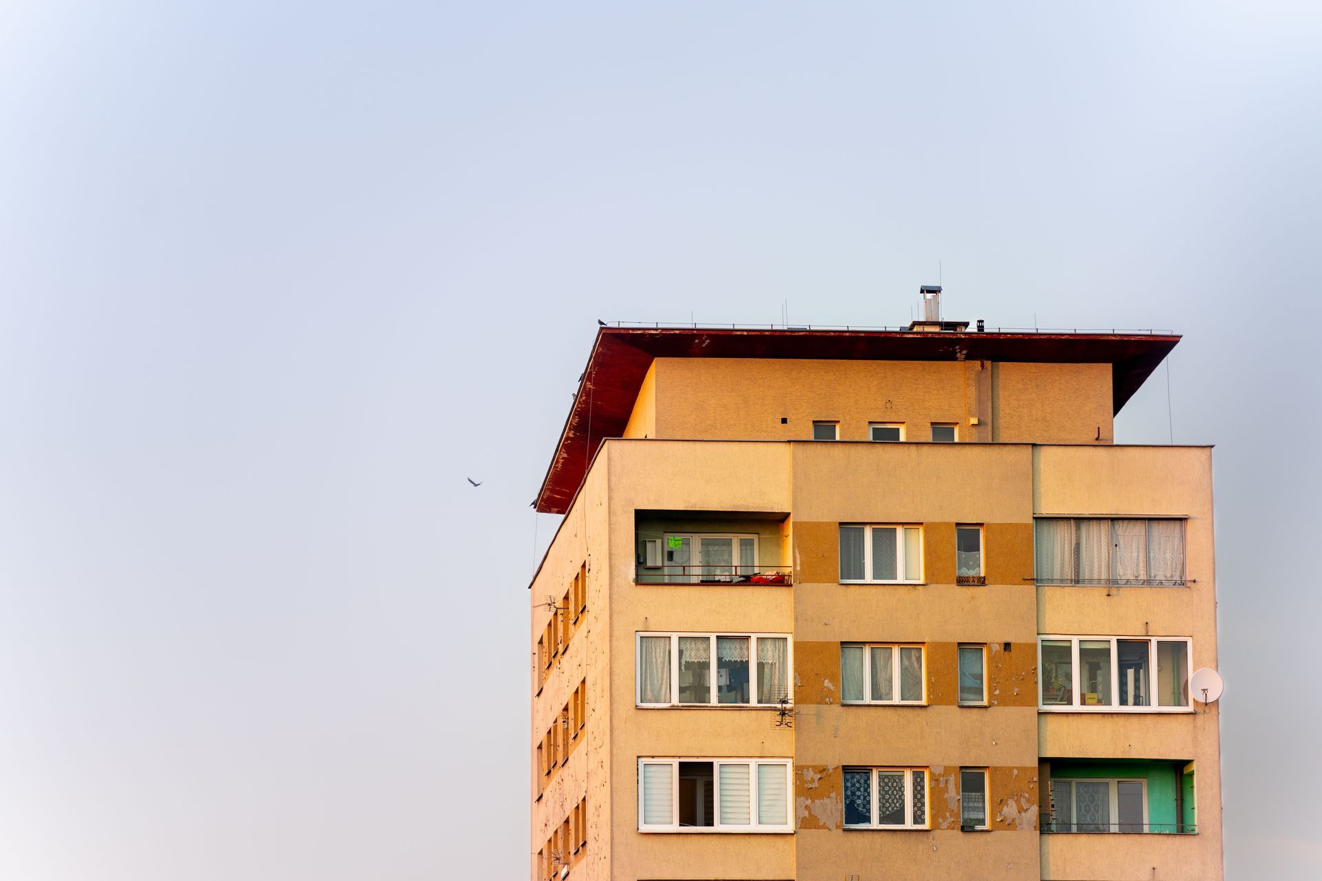 Tall beige apartment building with balconies against a pale blue sky