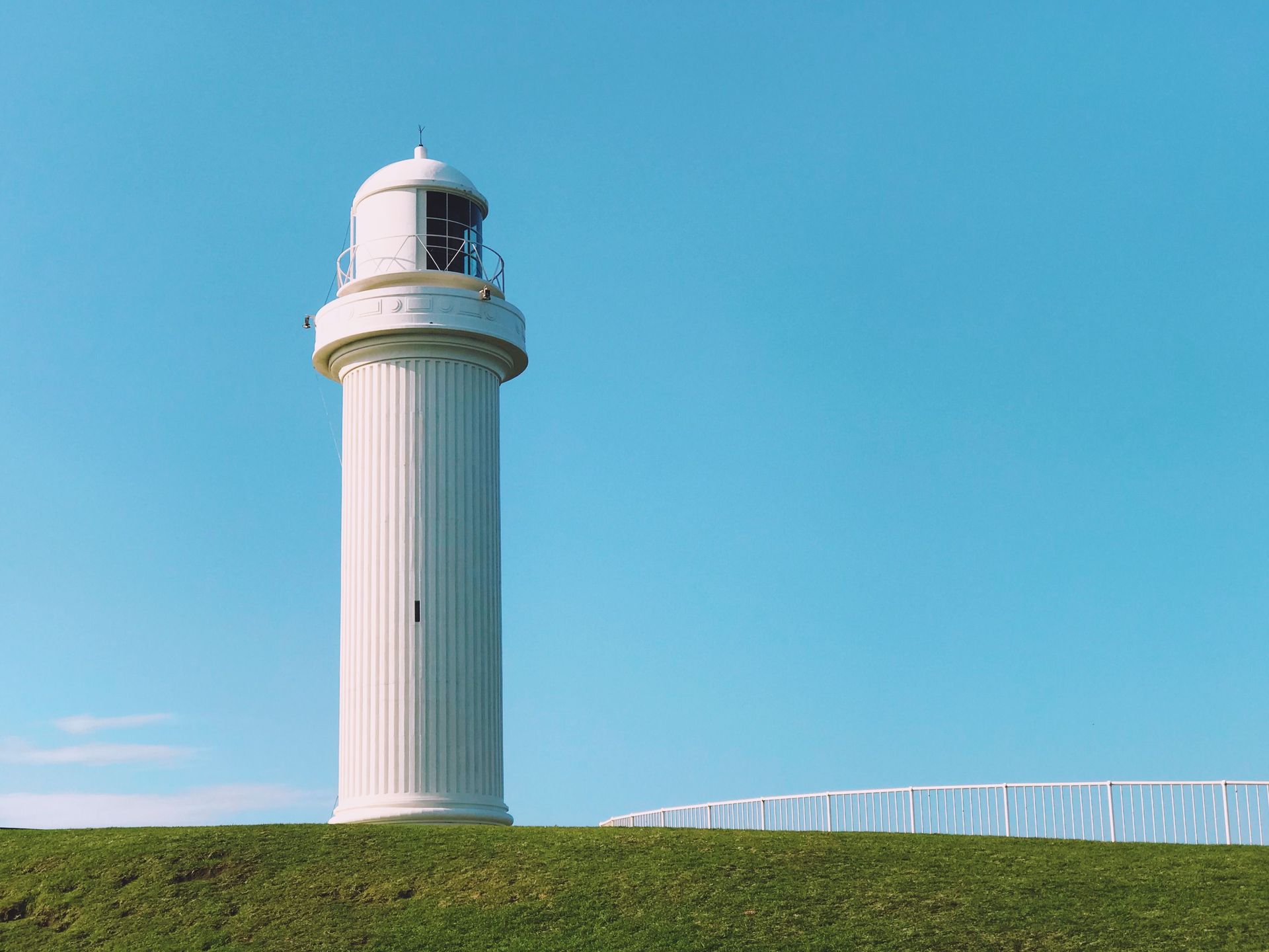 White lighthouse against a clear blue sky on a grassy hill