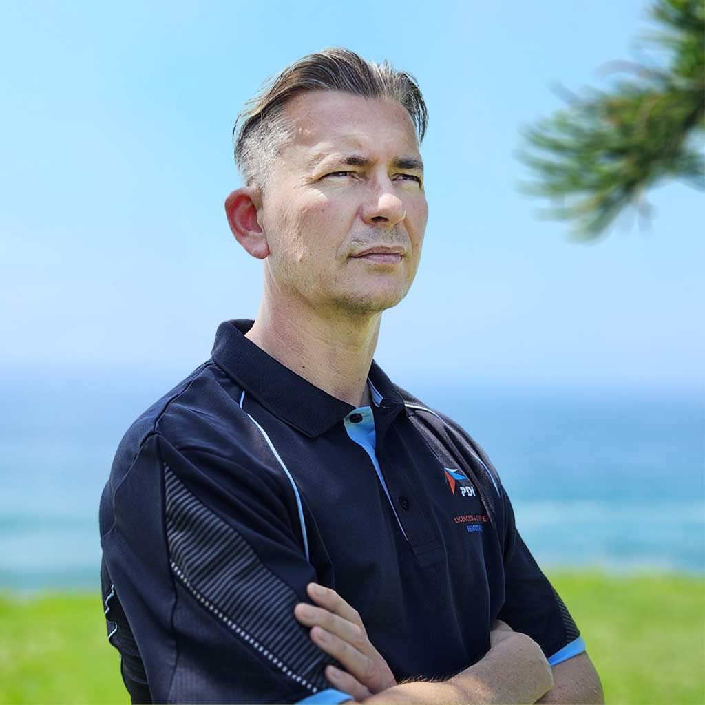 Photo of man with dark grey short hair with blue sky and ocean background Daniel James 