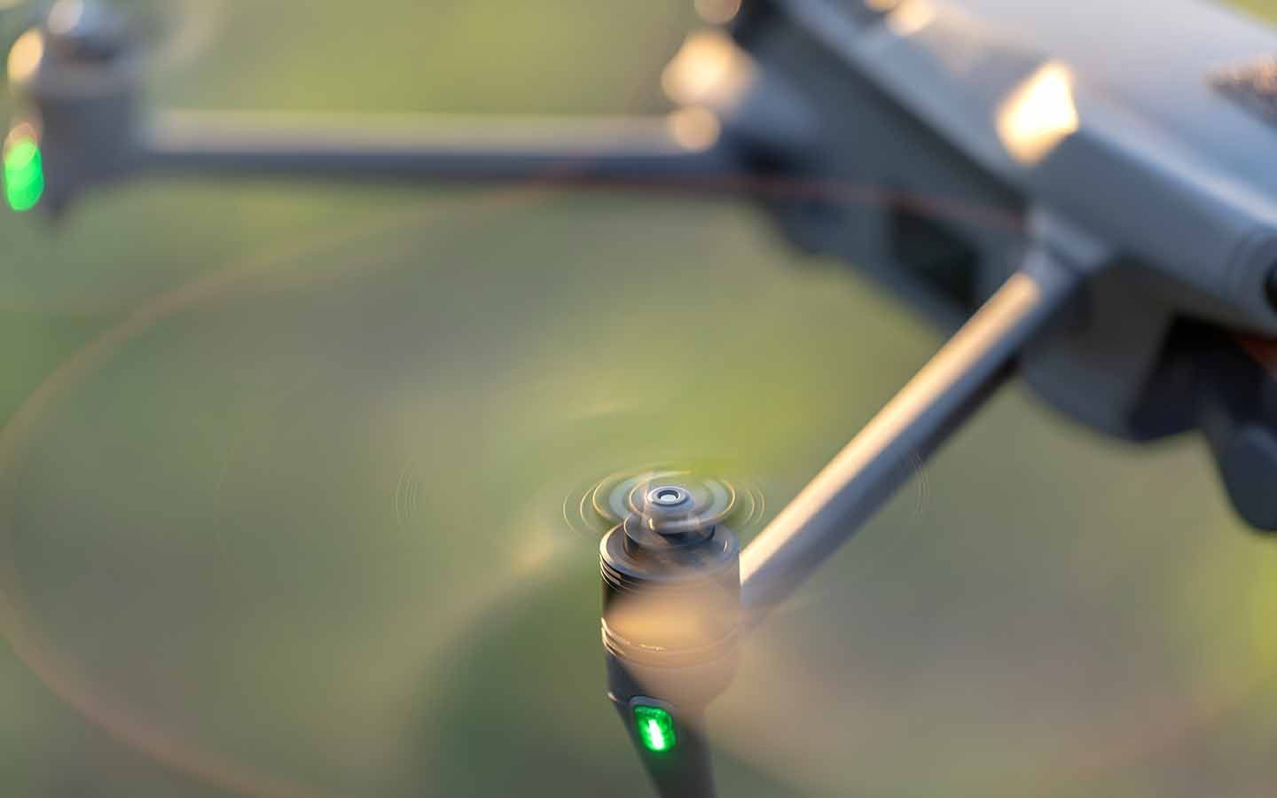 Close-up of a gray drone propeller and motor with a green navigation light against a blurred background