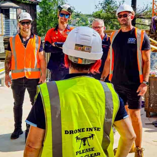 Female drone pilot in PPE talking to construction workers on site 