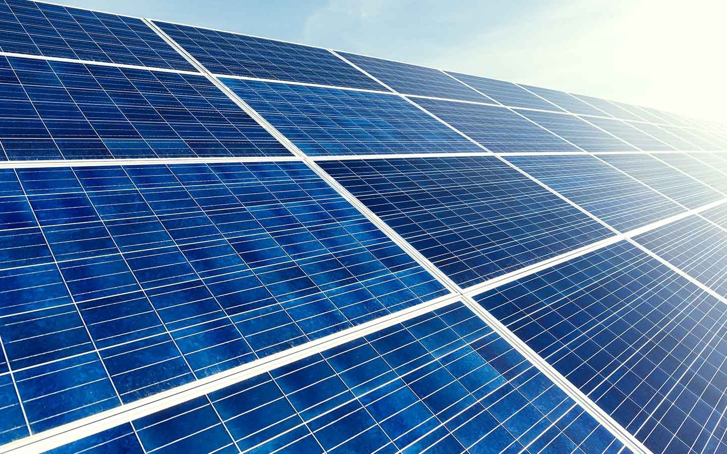 Rows of blue solar panels under bright sunlight, angled across a rooftop solar panels.
