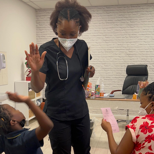 female doctor with stethoscope around her neck high fiving children in doctors room