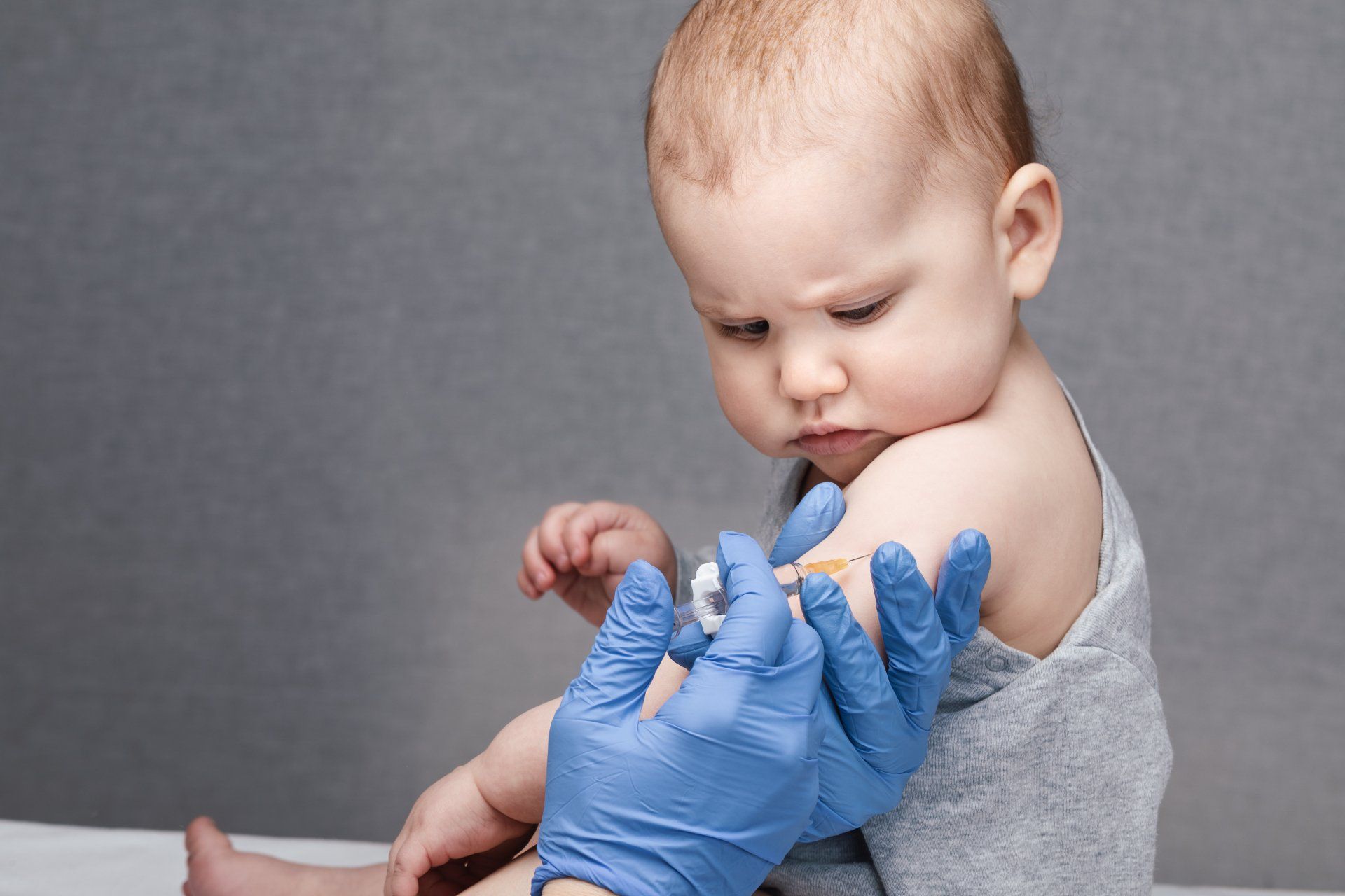 Adult hands in protective gloves injecting a baby's arm