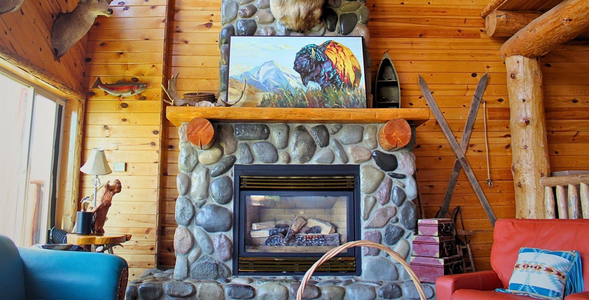 A living room with a fireplace and a painting of a buffalo on the mantle.