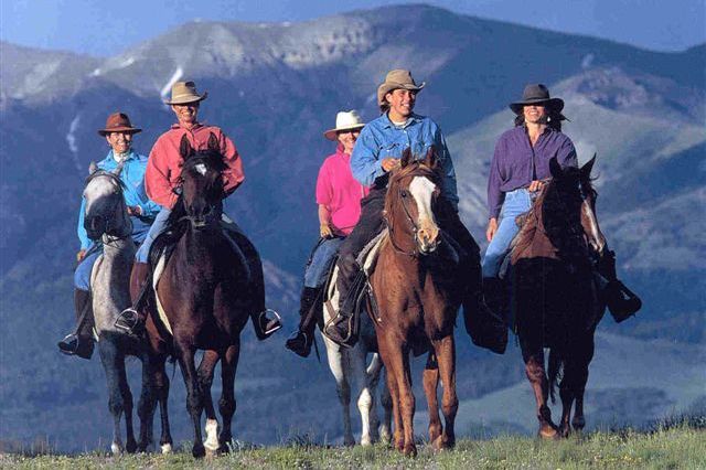 A group of people are riding horses in a field with mountains in the background