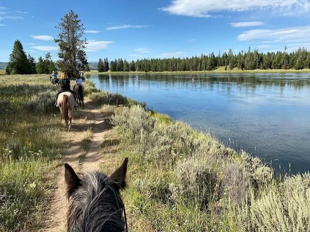 Two men are riding horses down a hill next to a river.