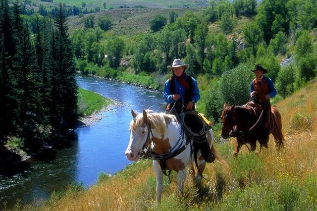 Two men are riding horses down a hill next to a river.