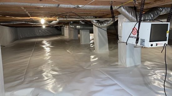 Crawlspace under house lined with white vapor barrier, exposed beams, ducts, and a small monitor on a support post