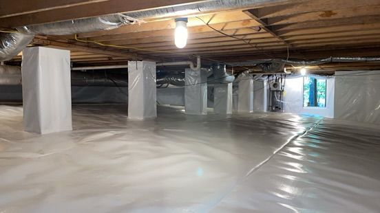 Crawlspace with plastic-covered floor, wooden beams, support posts, and a single light bulb hanging overhead