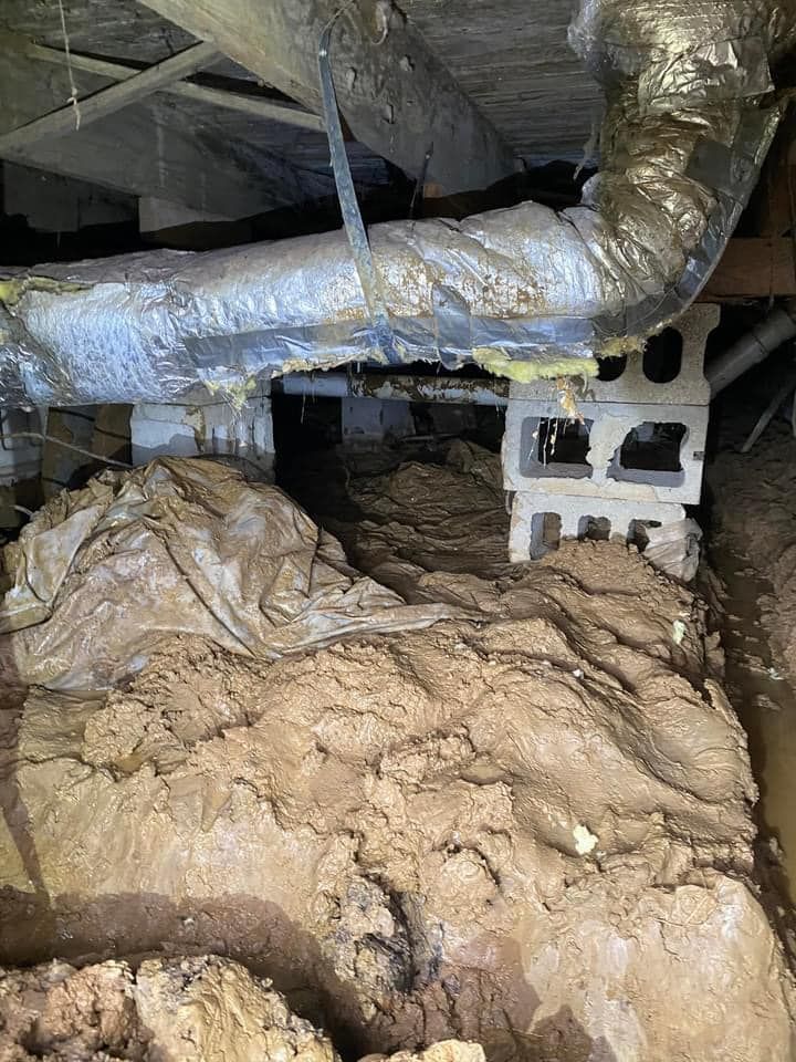 Insulated ductwork and exposed pipes in a crawl space with dirt floor and cinder blocks
