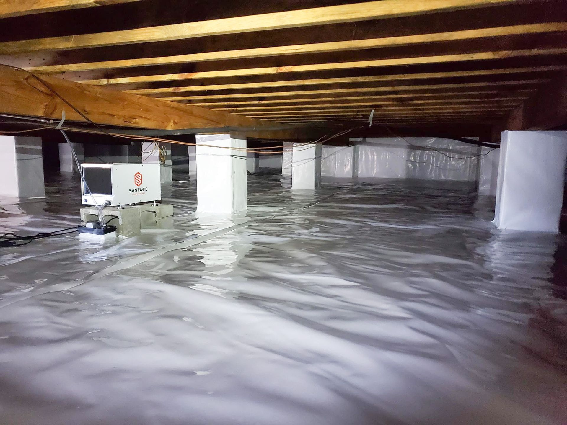 Flooded crawl space under a house with standing water and exposed wooden beams