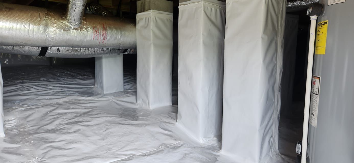 Crawlspace with white vapor barrier on floor and wrapped ductwork and pipes overhead
