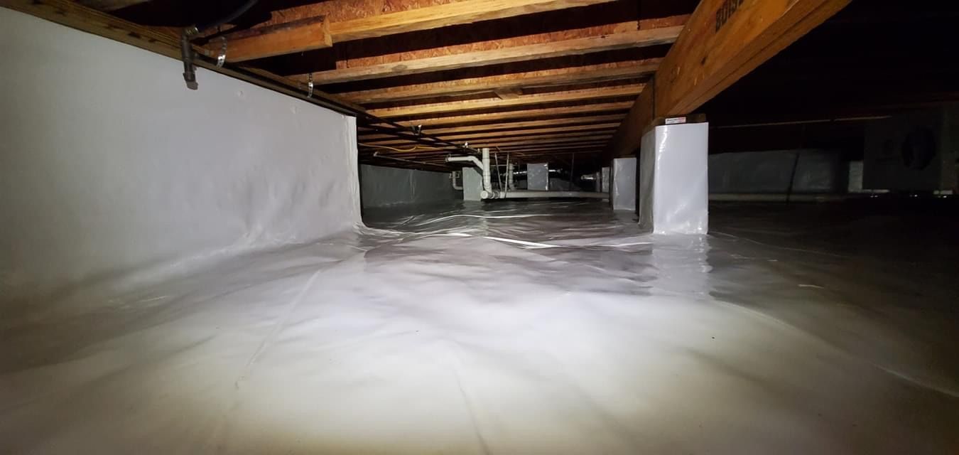 Crawlspace with exposed wooden beams, white insulation, and a thick layer of snow or foam on the floor