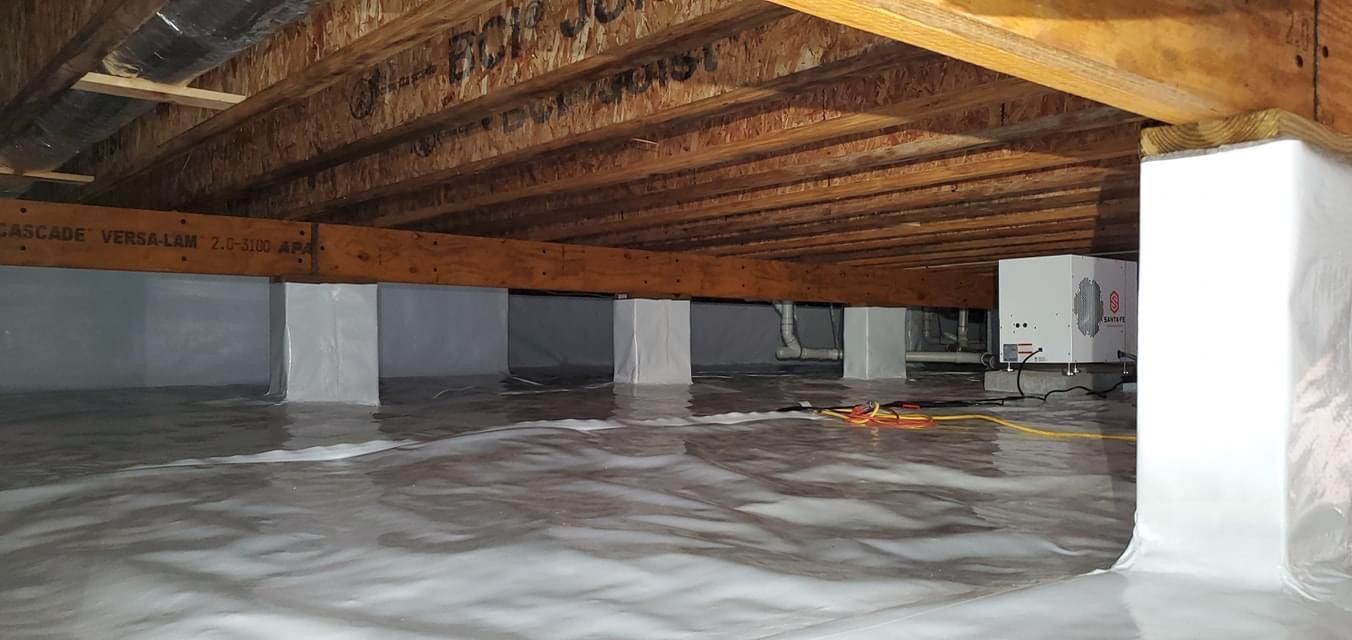 Interior of a crawlspace with exposed wooden beams, white support columns, and a plastic vapor barrier on the floor