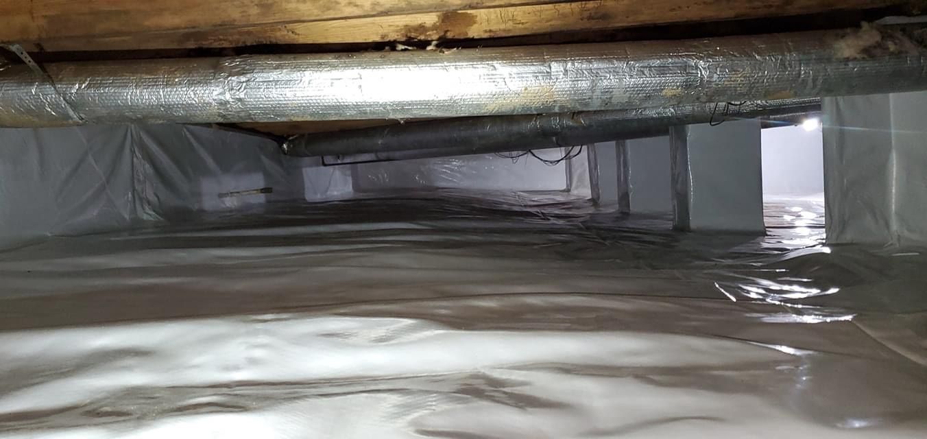 Inside a crawlspace, plastic sheeting covers the floor beneath wooden beams and insulation.