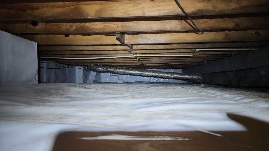 A low wooden crawlspace with exposed beams and a white insulated floor under a dark ceiling.