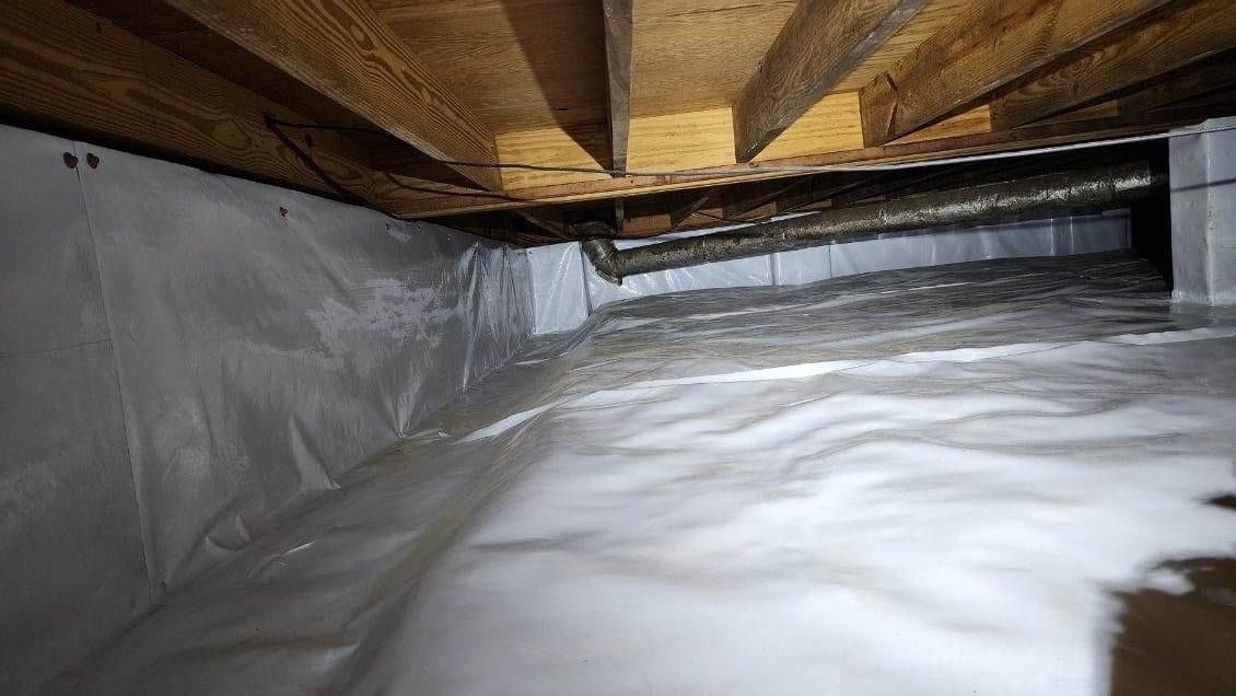 Insulated crawlspace with white plastic vapor barrier and wooden beams overhead