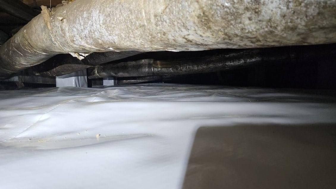 Close-up of insulation and white sheeting in a narrow crawlspace or attic gap