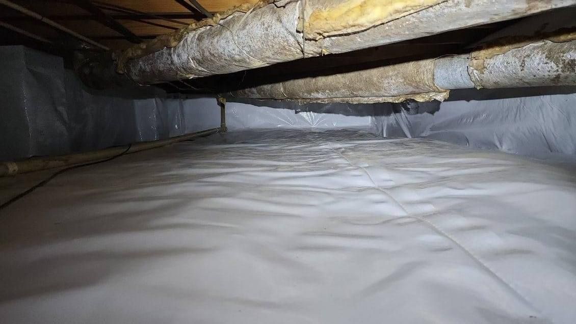 Insulated crawlspace with white vapor barrier on the floor and ducts overhead