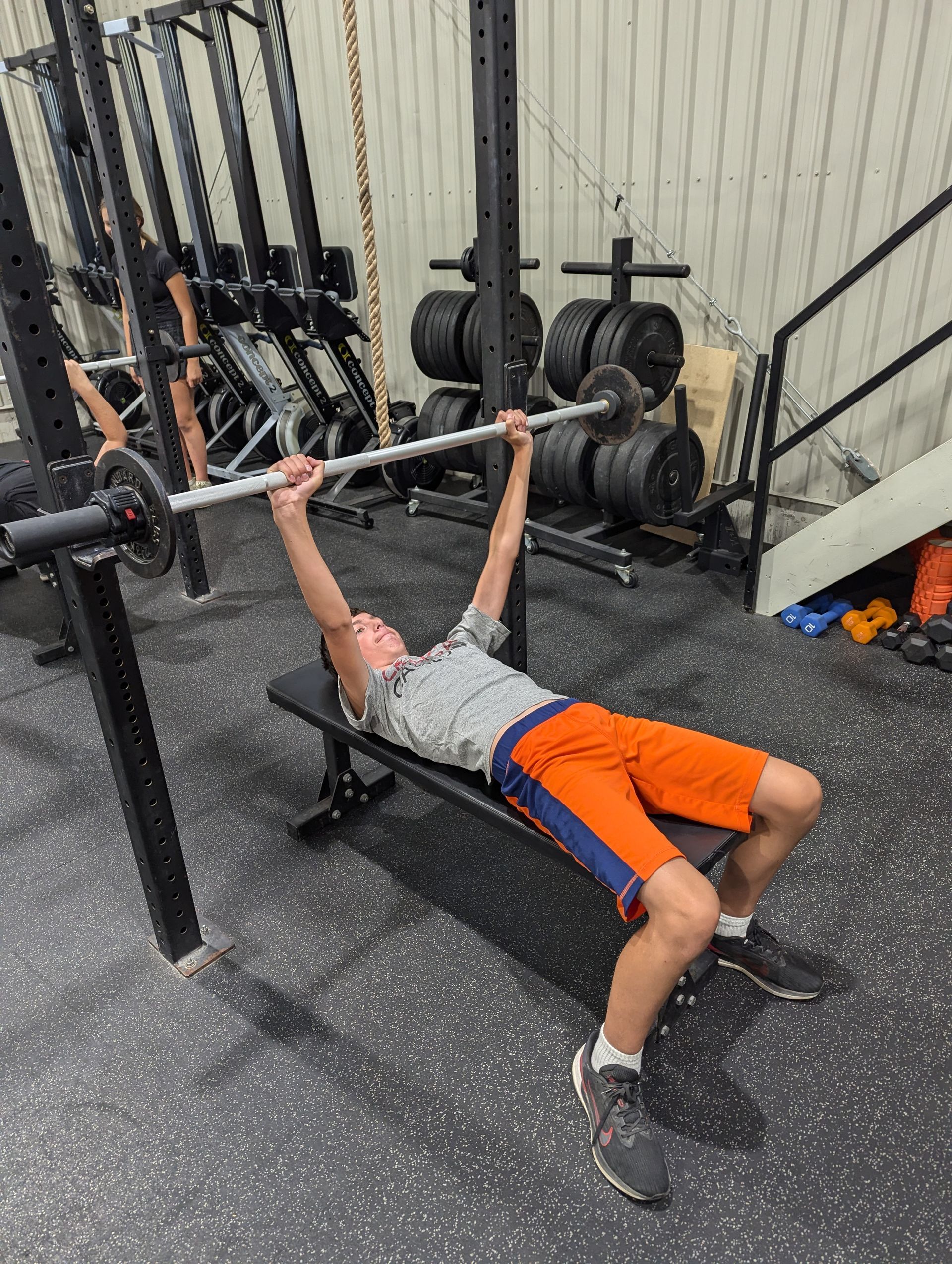 A young boy is lifting a barbell on a bench in a gym.