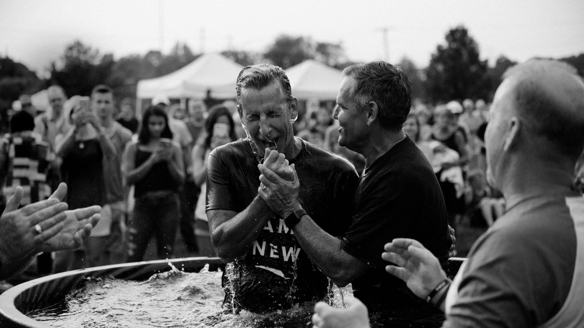 A black and white photo of a man being baptised by a group of people.