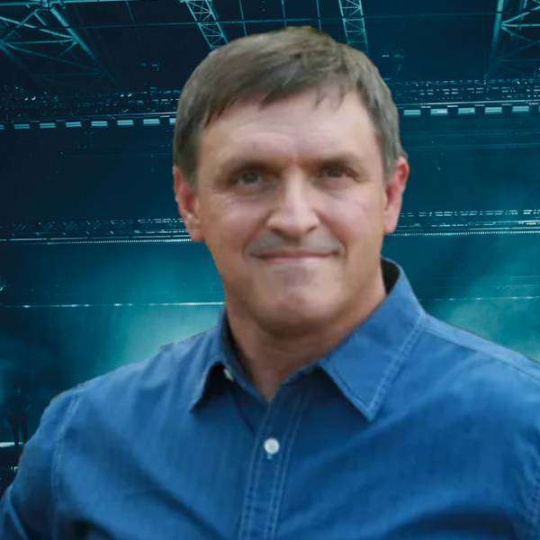 A man in a blue shirt is standing in front of a stadium.