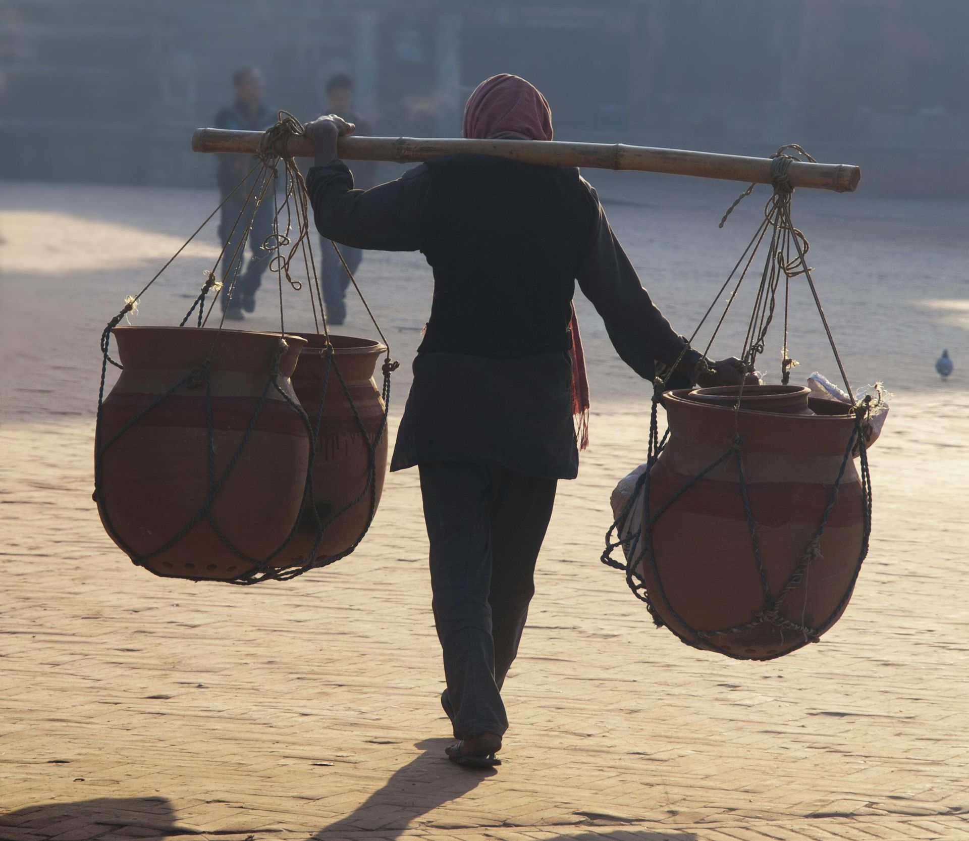 A person is carrying two pots on their shoulders