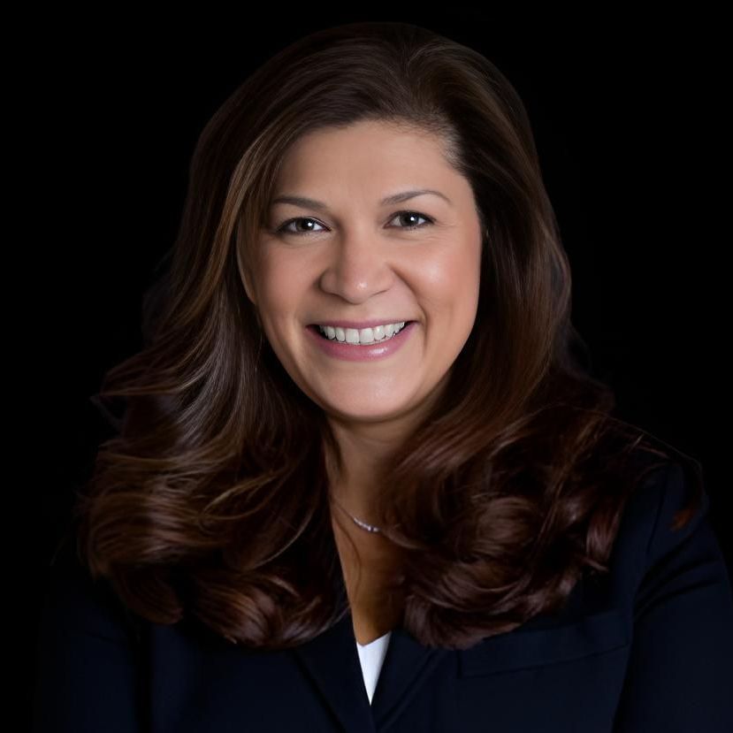 A woman with long brown hair is smiling and wearing a black jacket.