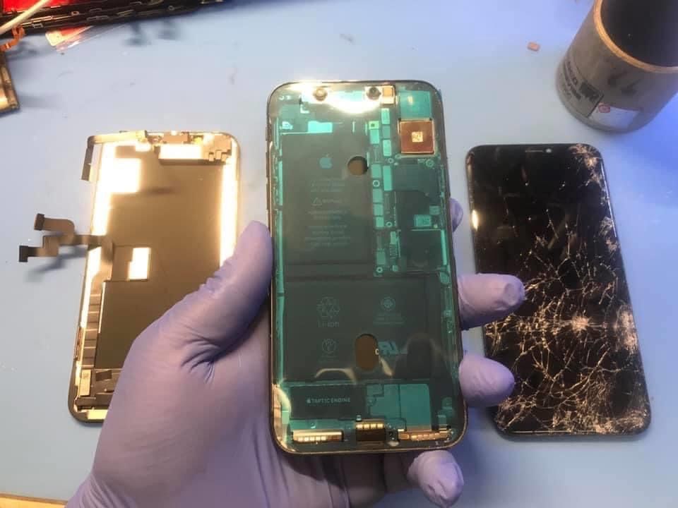 A person wearing purple gloves is holding a phone with the back removed