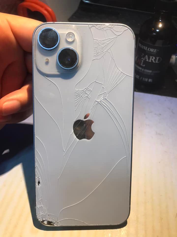 A person is holding a white iPhone with a broken back cover.