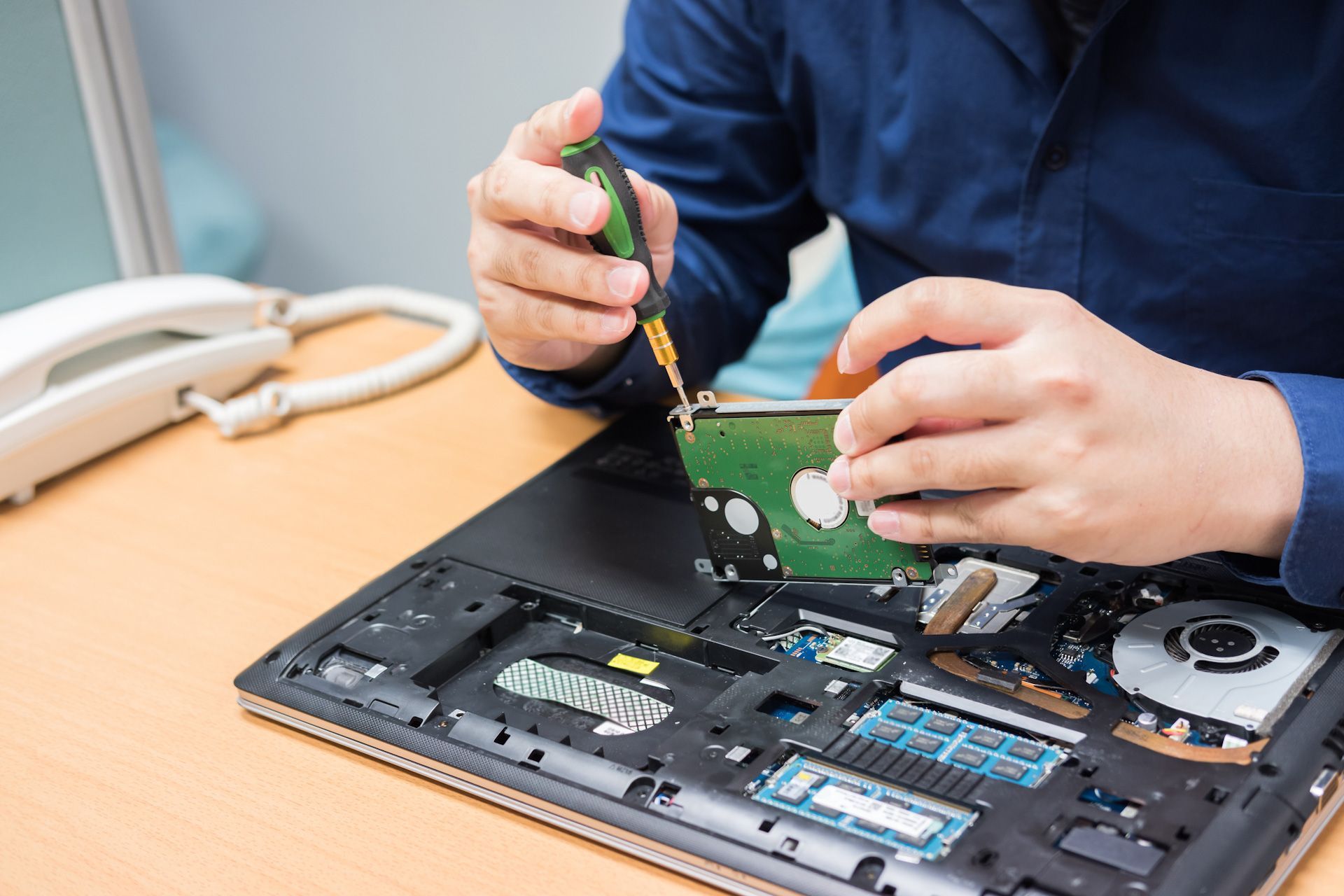 A man is fixing a laptop computer with a screwdriver.