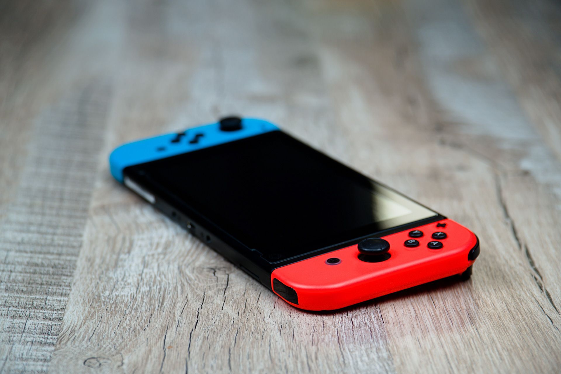A red and blue Nintendo Switch is sitting on a wooden table.