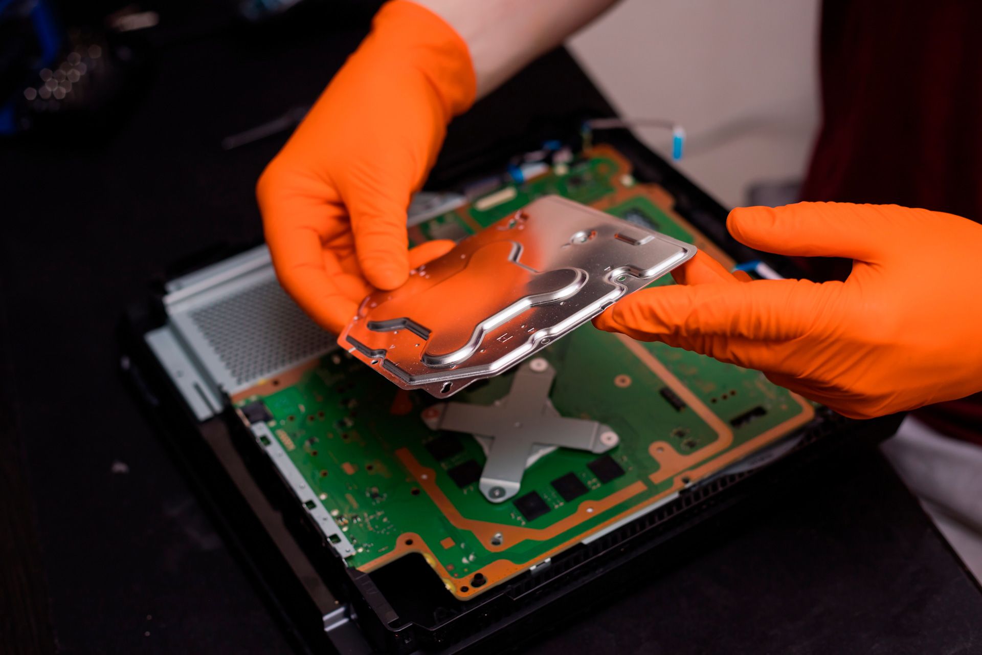 A person wearing orange gloves is holding a hard drive in their hands.