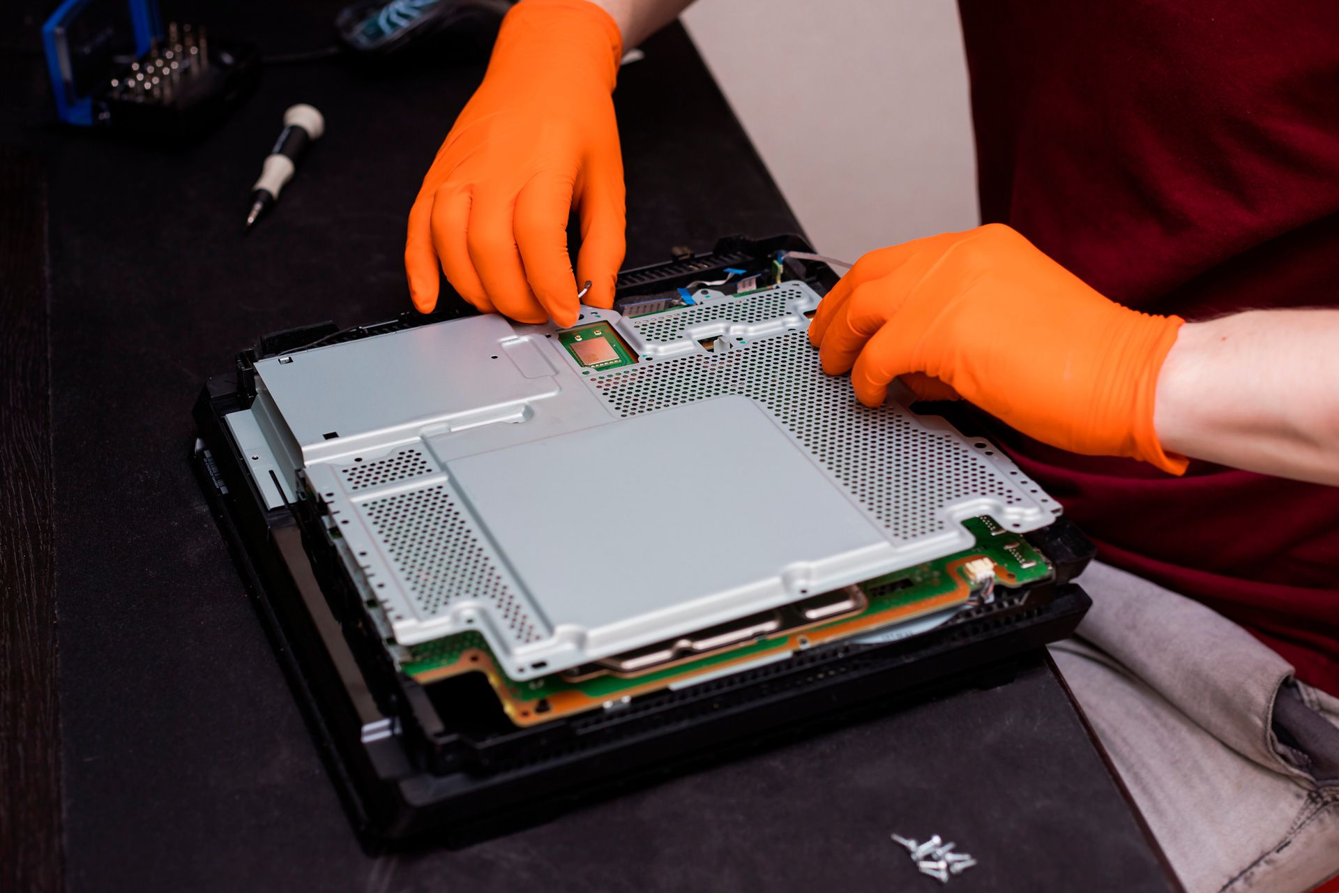 A person wearing orange gloves is working on a PlayStation.