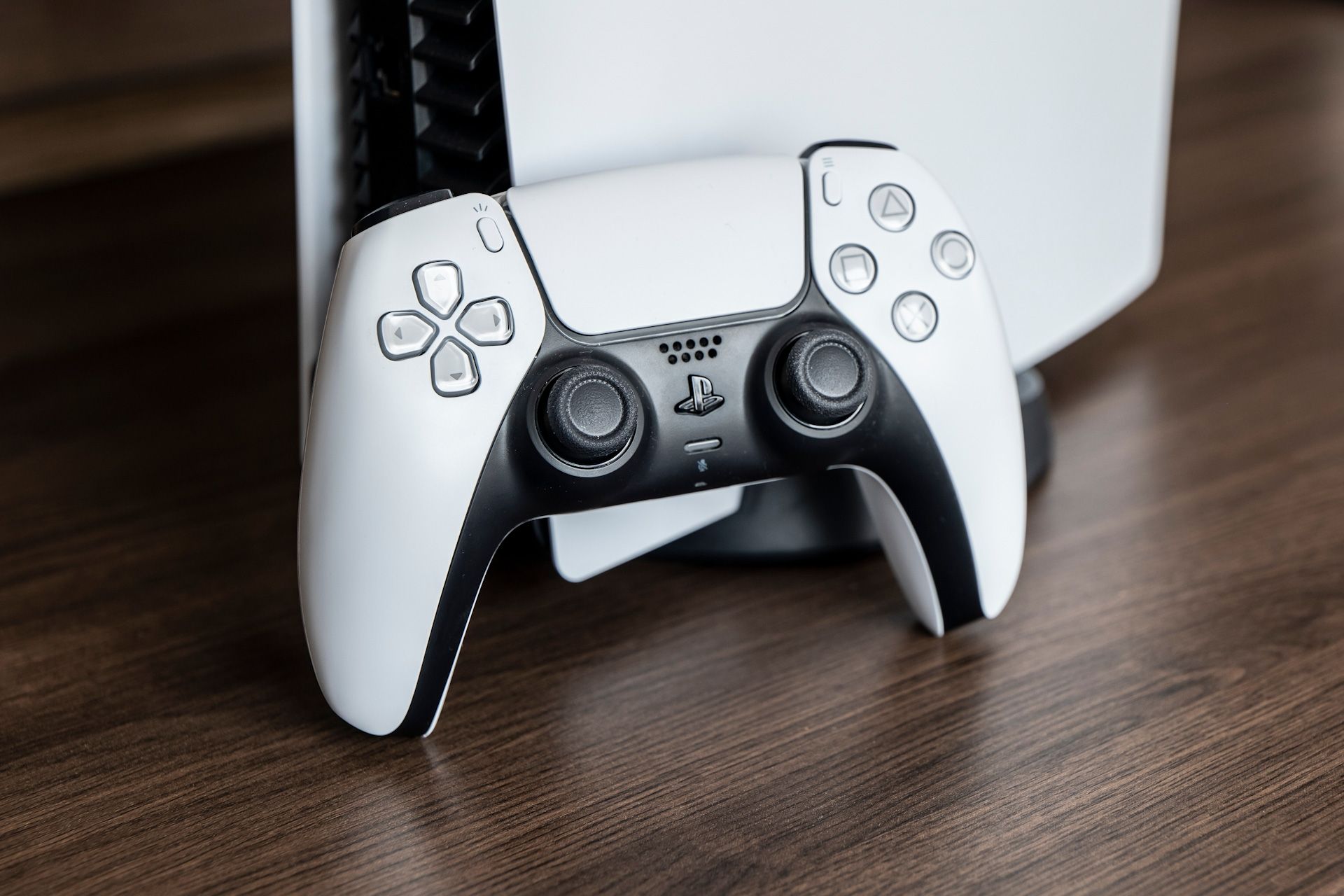 A white and black PlayStation controller is sitting on a wooden table.