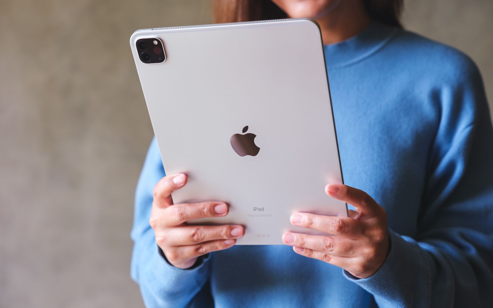 A woman in a blue sweater is holding an iPad in her hands.