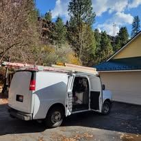 A white van with a ladder on top of it is parked in front of a garage.