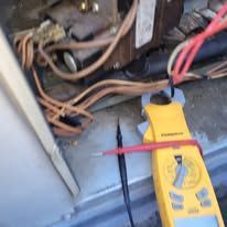A yellow multimeter is sitting on top of a metal surface next to a bunch of wires.