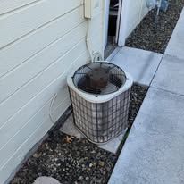 An air conditioner is sitting on the side of a house next to a sidewalk.