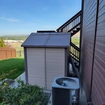 A small shed is sitting on the side of a house next to an air conditioner.