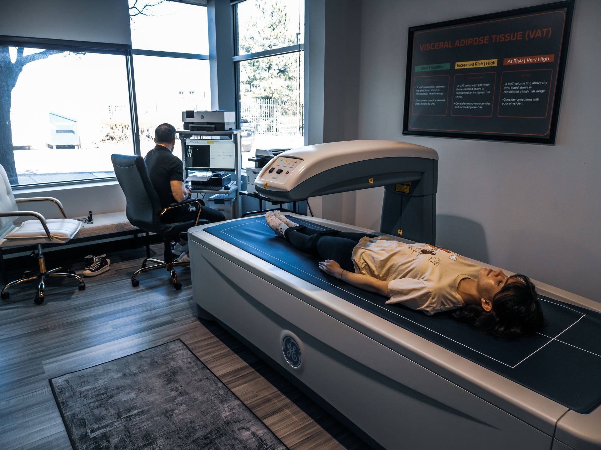 A doctor is using a computer while a patient is laying on a bed