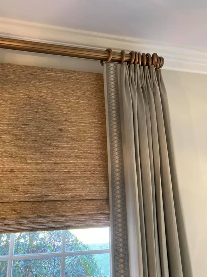 A close up of a window with curtains and a wooden curtain rod.