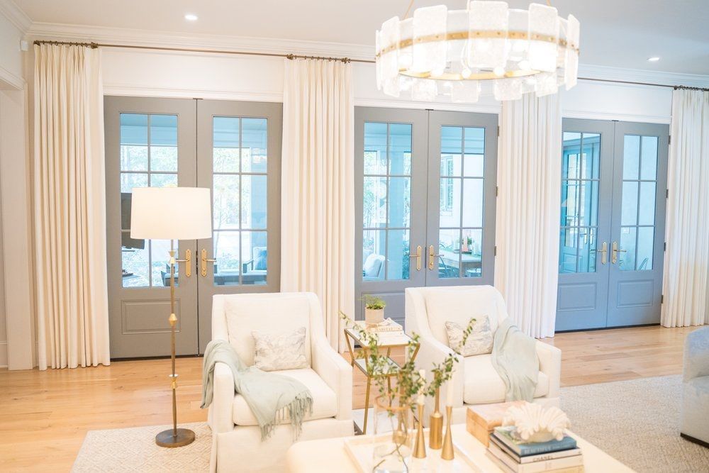 A living room filled with furniture and a chandelier and custom drapes over the doors.