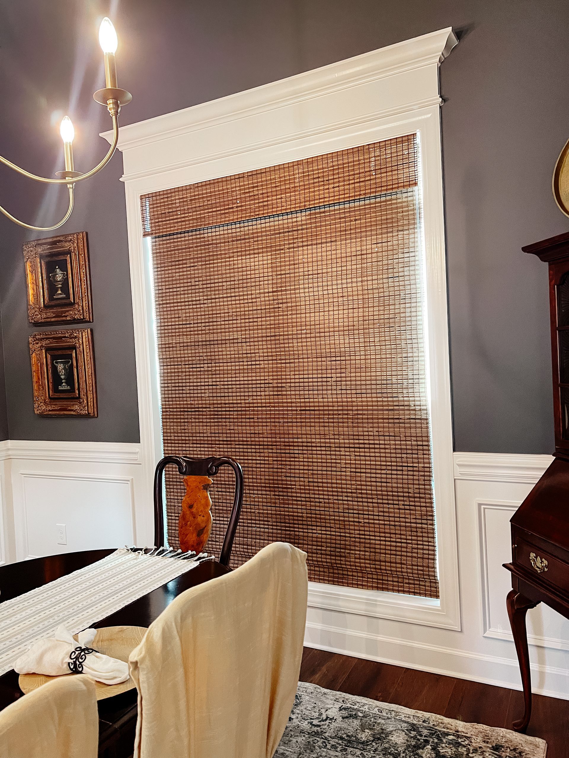 A dining room with a table and chairs and a clock and a natural woven shade on the window.