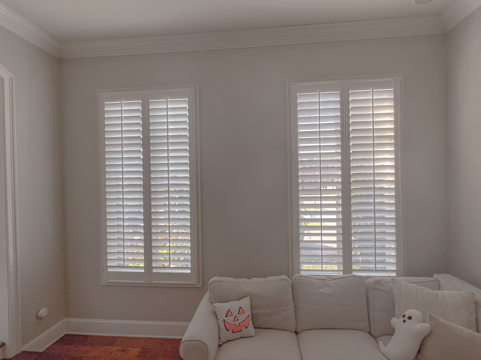 A living room with a couch and two windows with shutters.